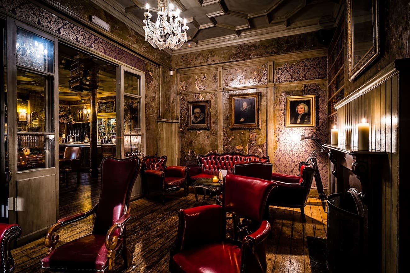 A candlelit London bar: red leather armchairs, a chandelier and old portraits on damask walls.